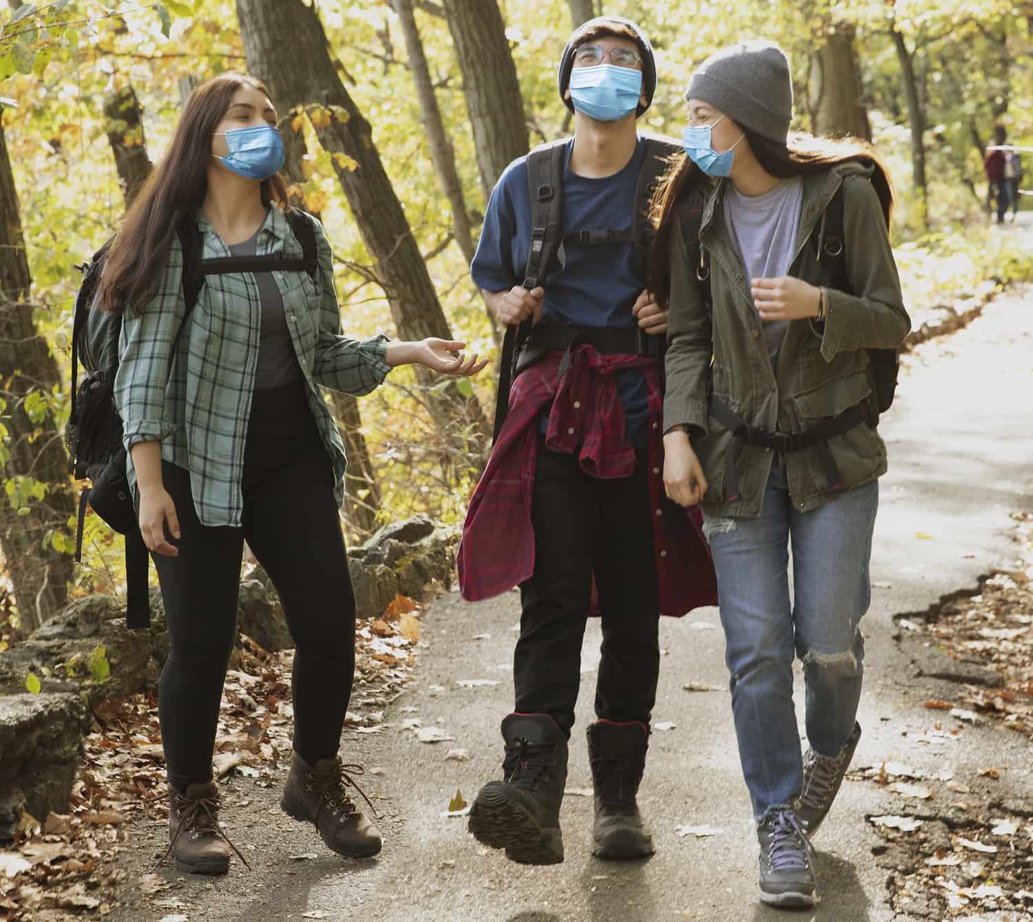 Three teens wearing masks hike through the woods.